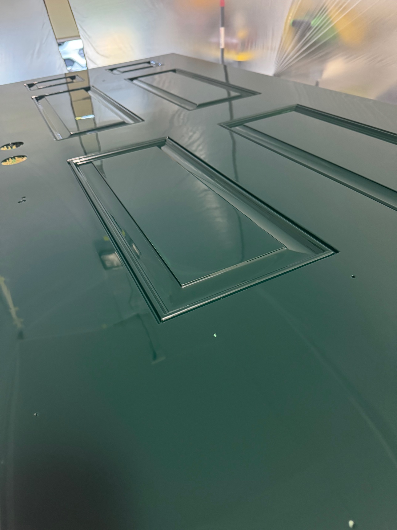 The door flat in the booth in deep green high gloss, the finish sweeping across its raised panels