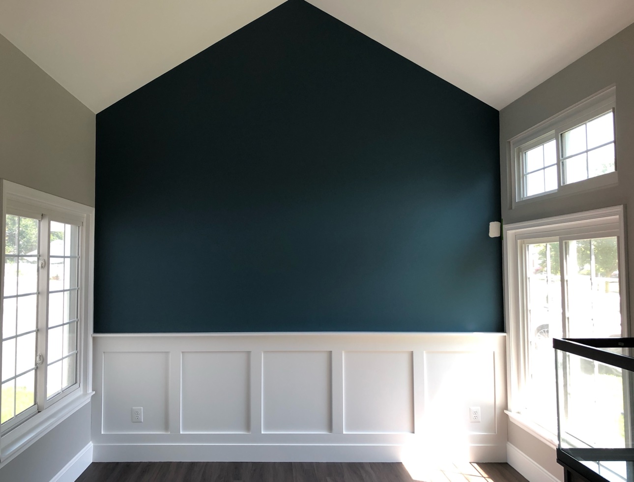 Finished room with a deep teal gable accent wall above white wainscoting, vaulted ceiling and tall windows