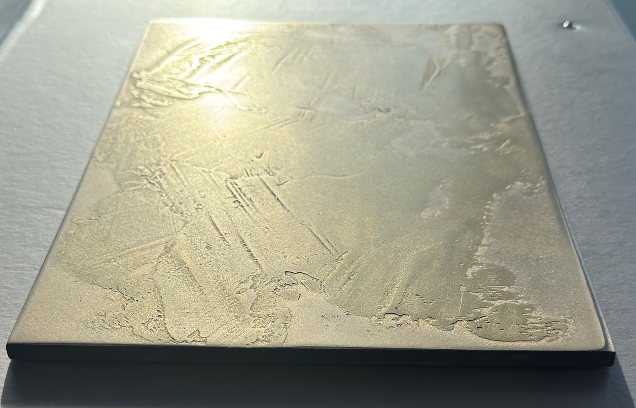 Liquid metal sample board photographed at a low raking angle in daylight, its textured trowel work catching the light